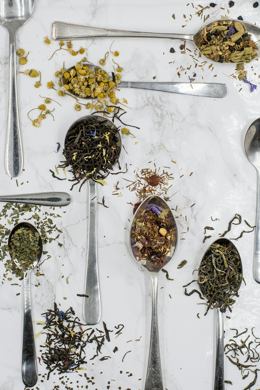 Various tea leaves and herbs on silver spoons